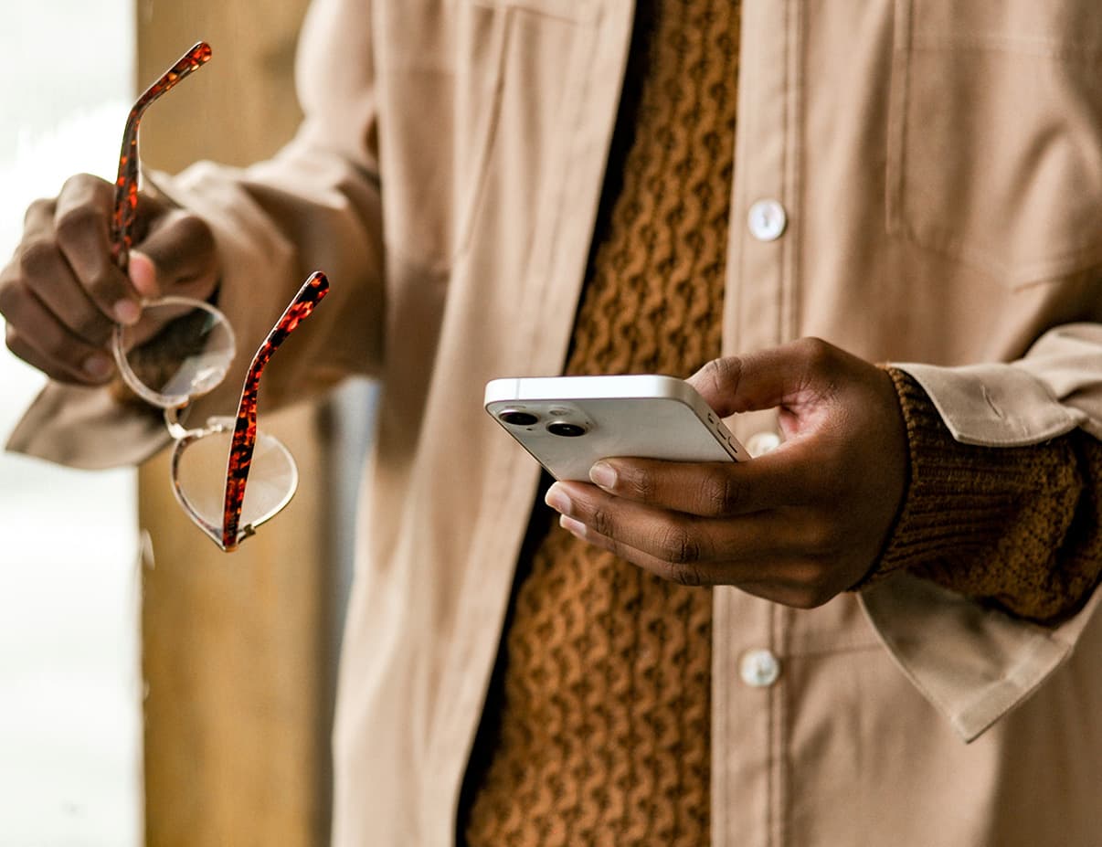 Close-up of a person holding a smartphone and tortoiseshell glasses while checking a prescription order