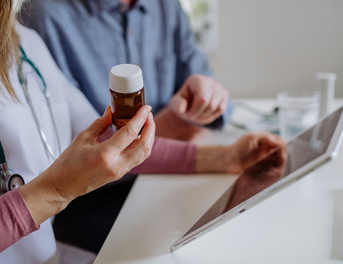 Pharmacist holding a medication bottle while reviewing product details on a tablet