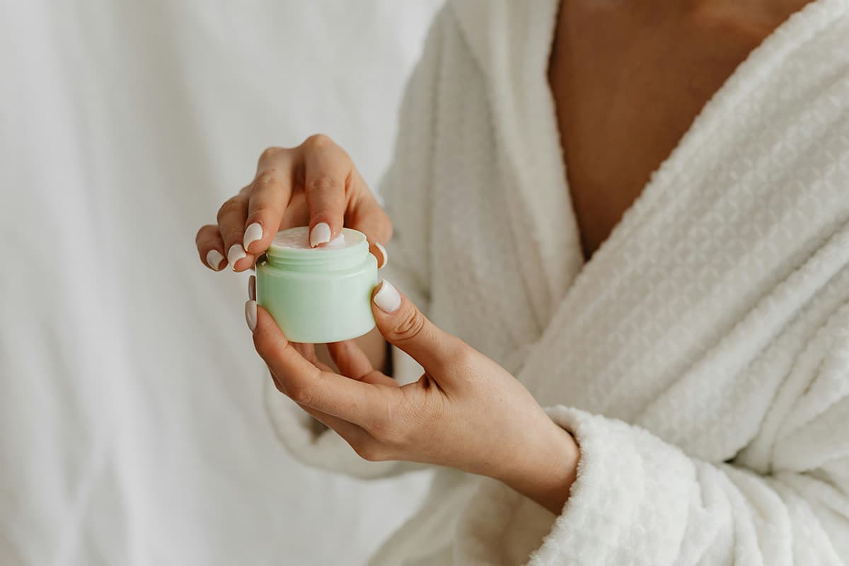 Woman in white spa robe opening a jar of prescription skincare cream
