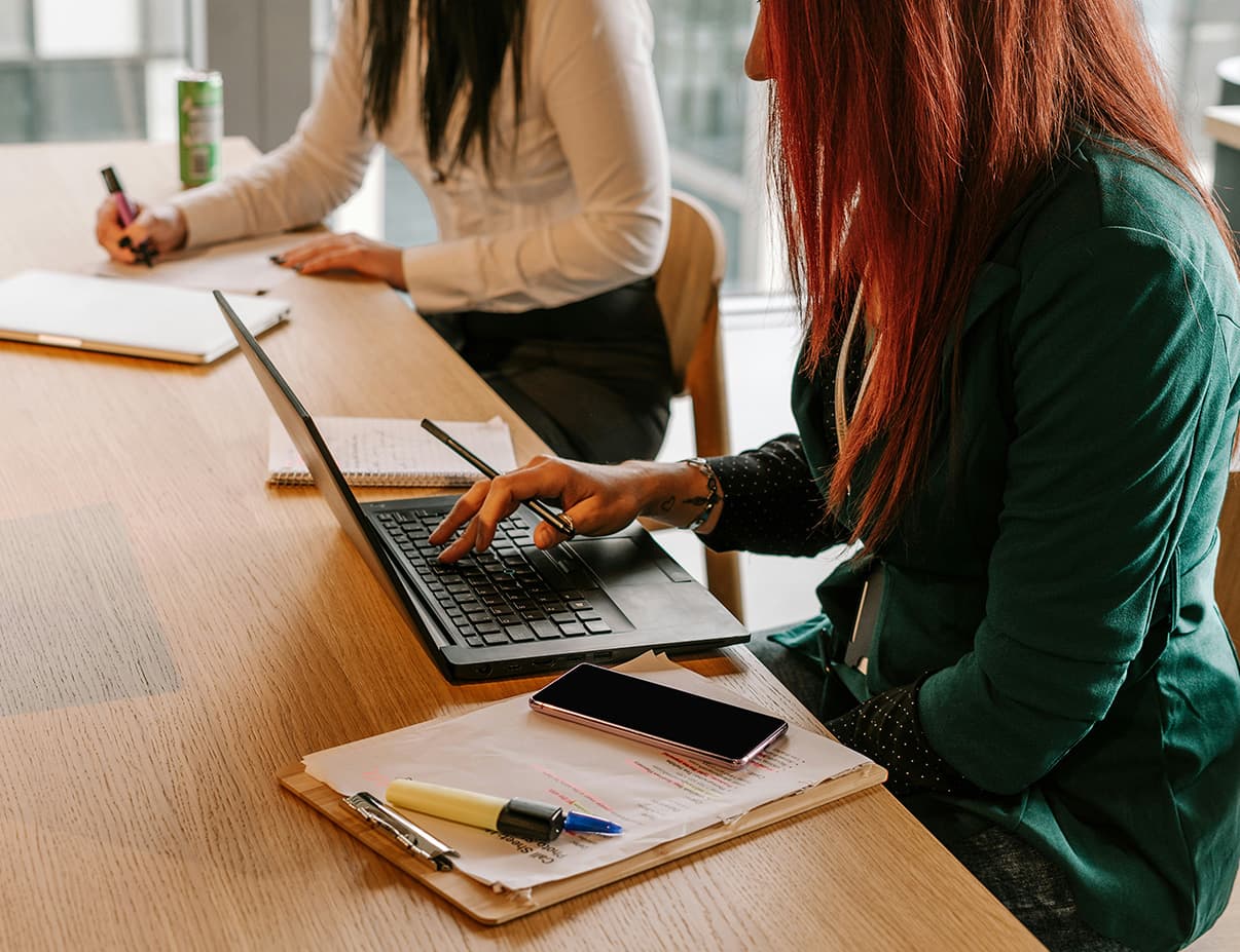 Two clinical office workers reviewing compliance documentation at a desk
