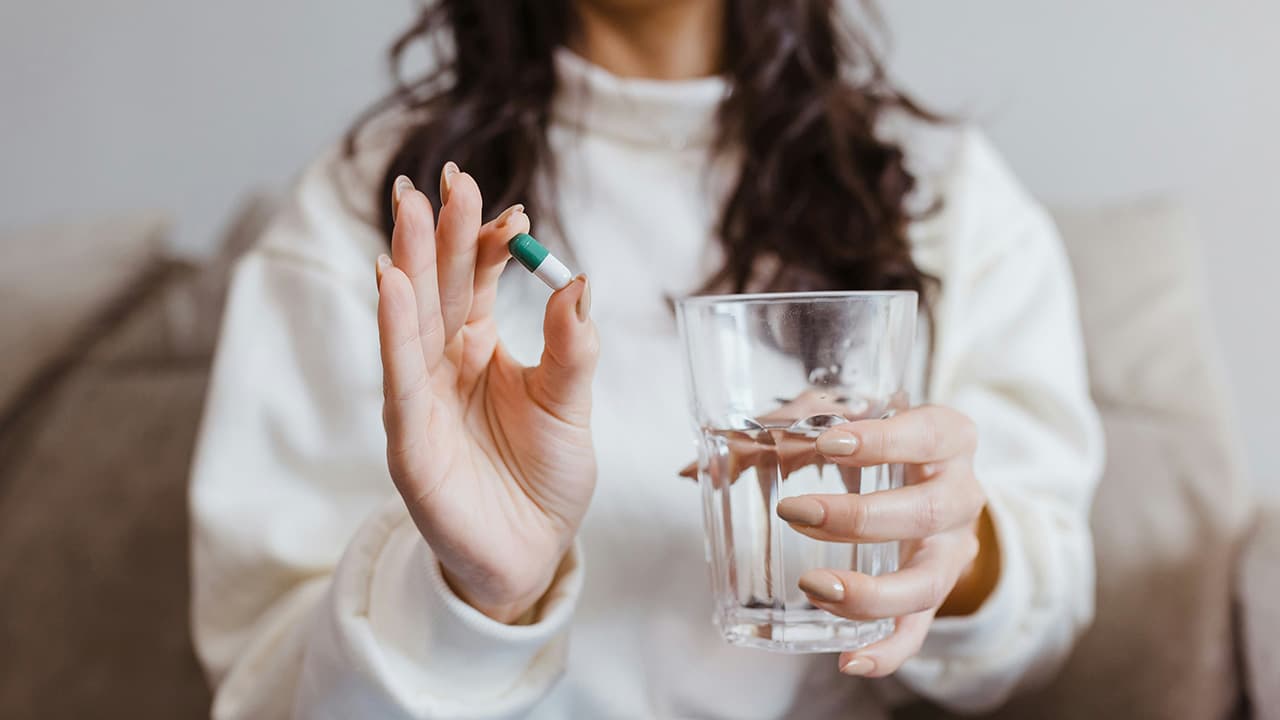 Woman holding a prescription capsule and glass of water