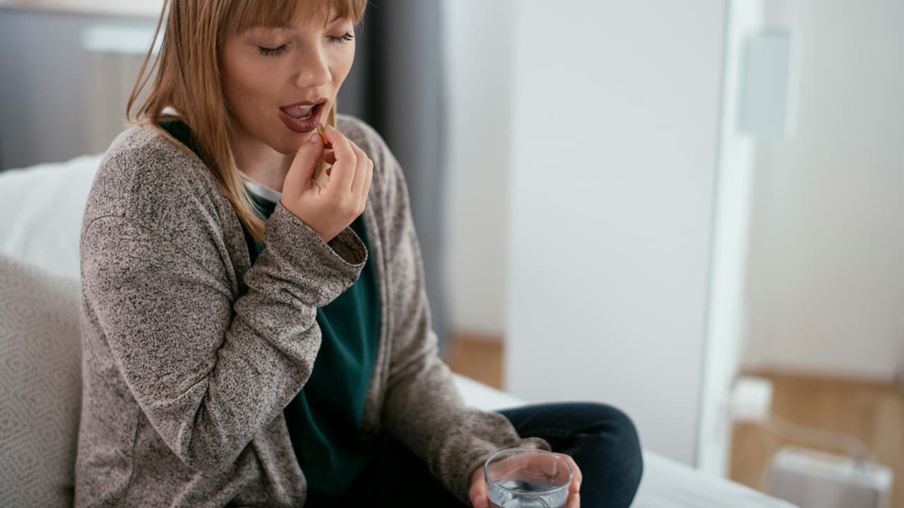 Woman taking prescription medication while sitting on her couch