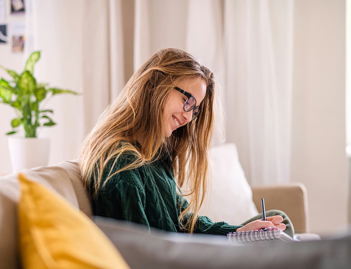 Woman in glasses writing notes on a couch while reviewing patient information