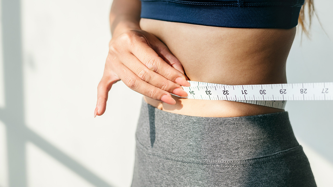 Woman measuring her waist with a tape measure after weight loss